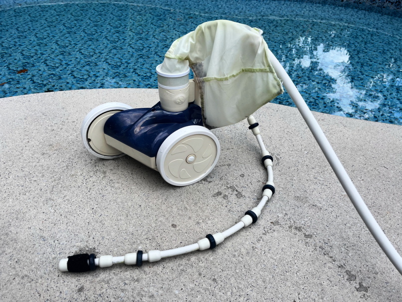 automatic swimming pool cleaner sitting by side of the pool
