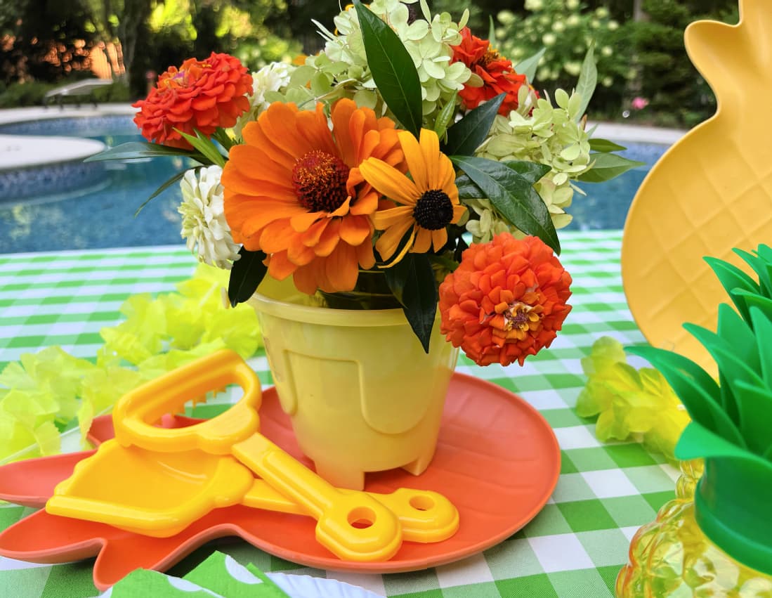 orange and yellow flowers in a sand pail for a Hawaiian pool party centerpiece