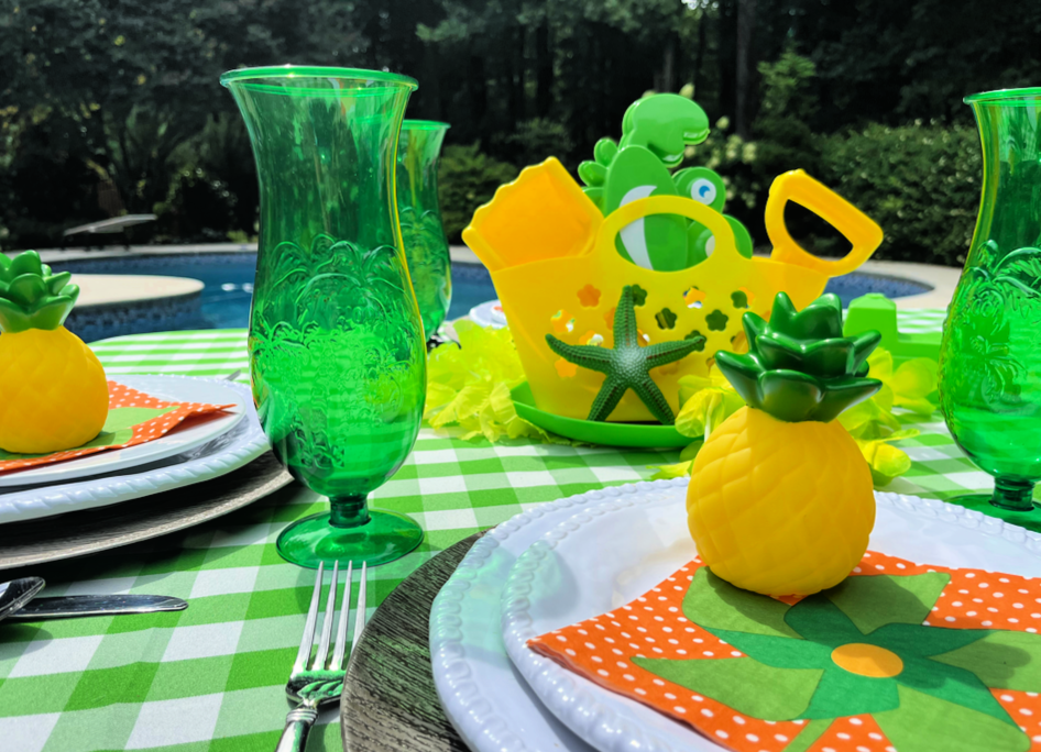pool party table with green outdoor glasses, white plates, and colorful centerpiece